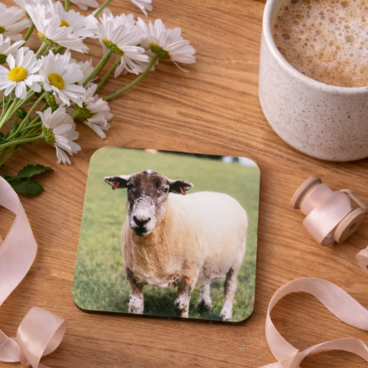 Coaster with a sheep design on a wooden tray with flowers and a cup of coffee.
